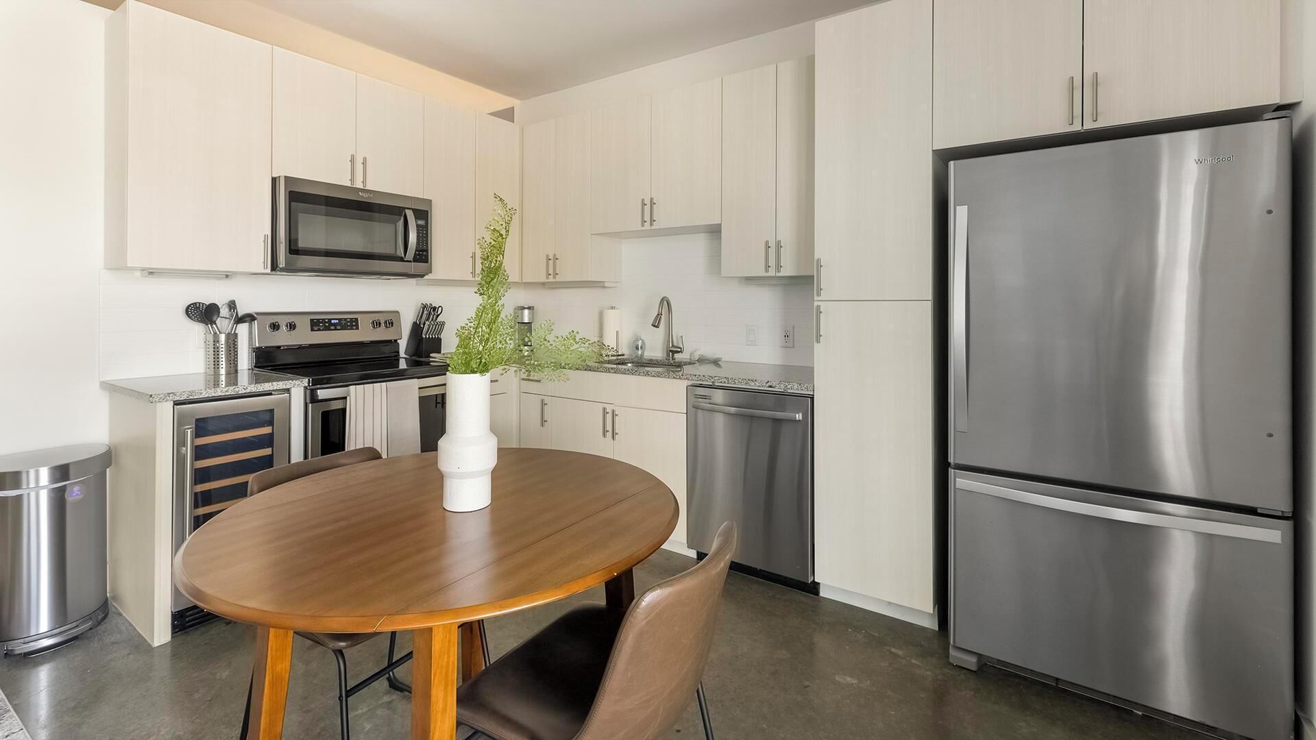 A modern kitchen with stainless steel appliances, a wooden dining table, and white cabinetry.
