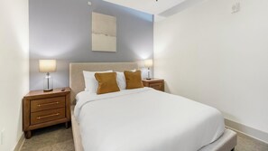 Ein ordentlich eingerichtetes Hotelzimmer mit einem großen Bett, Nachttischen und einem an der Wand hängenden Kunstwerk.
