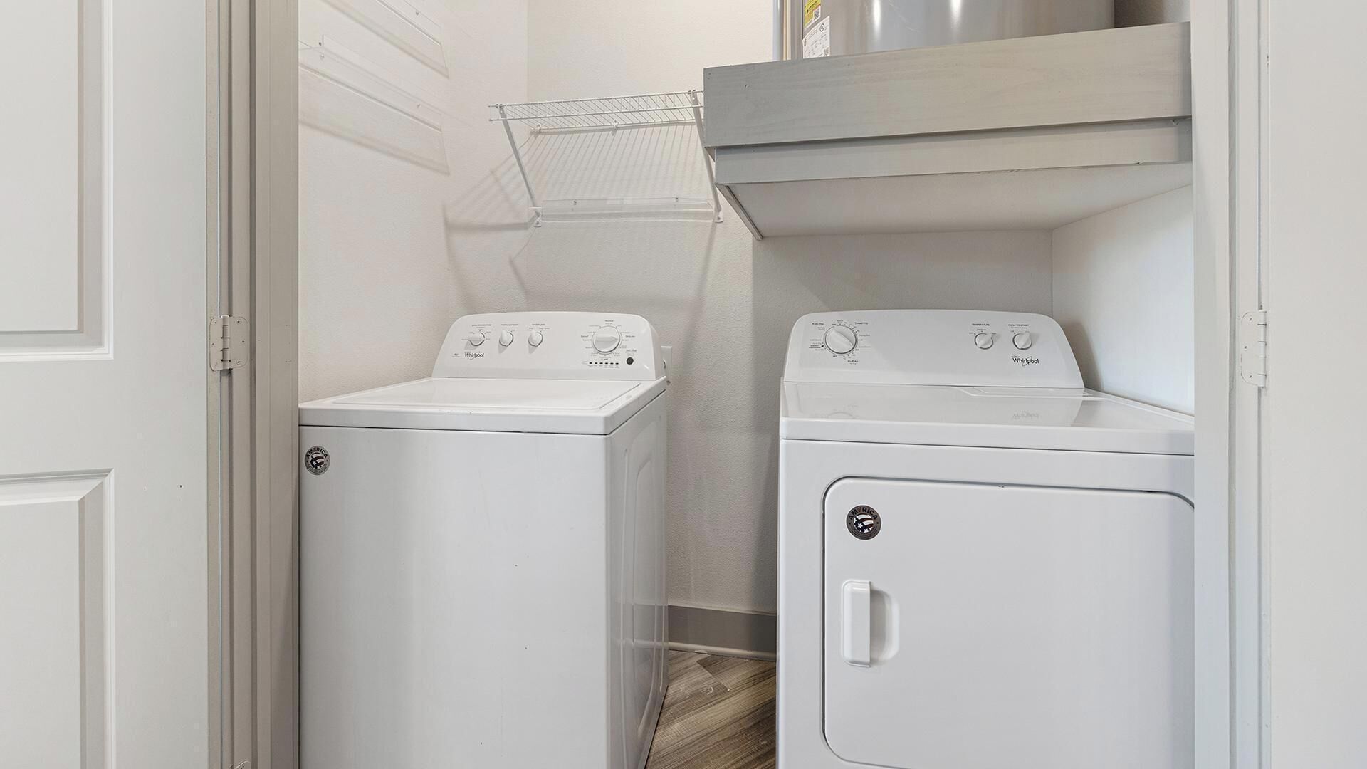 A laundry room with two white Whirlpool washers and dryers, a metal drying rack, and a white door.