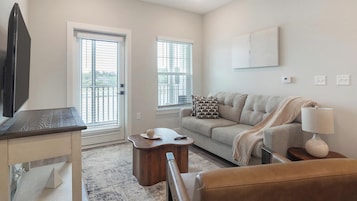 A living room with a sofa, a coffee table, a TV, and two windows with blinds.
