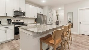 A modern kitchen with white cabinets, stainless steel appliances, a granite countertop, and wooden bar stools. - Landing Stylish 1bd, Gym (Beaufort)