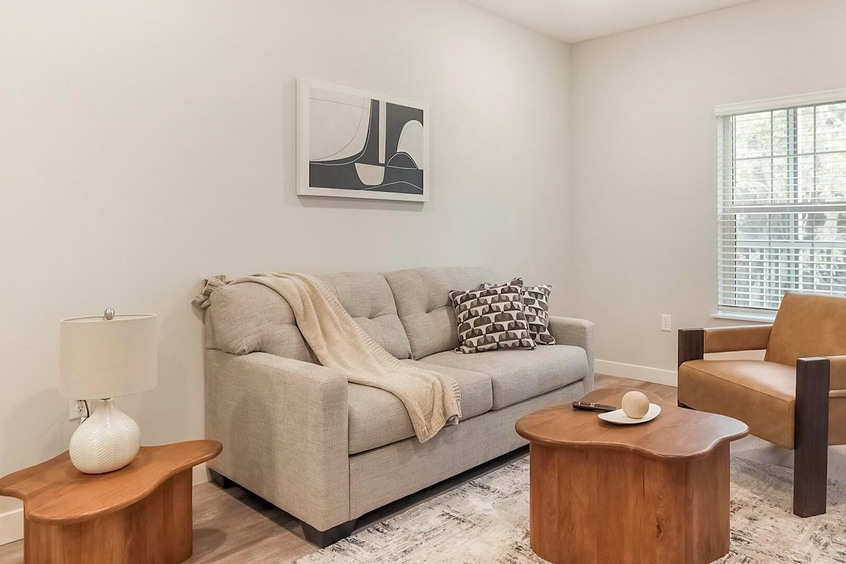 A living room with a sofa, a chair, a coffee table, a lamp, and a painting on the wall.