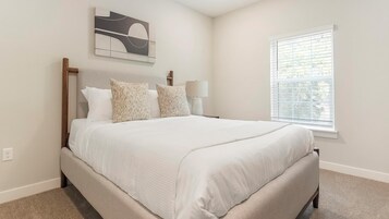 A bedroom with a bed, a nightstand, a lamp, a wall art piece, and a window with blinds.