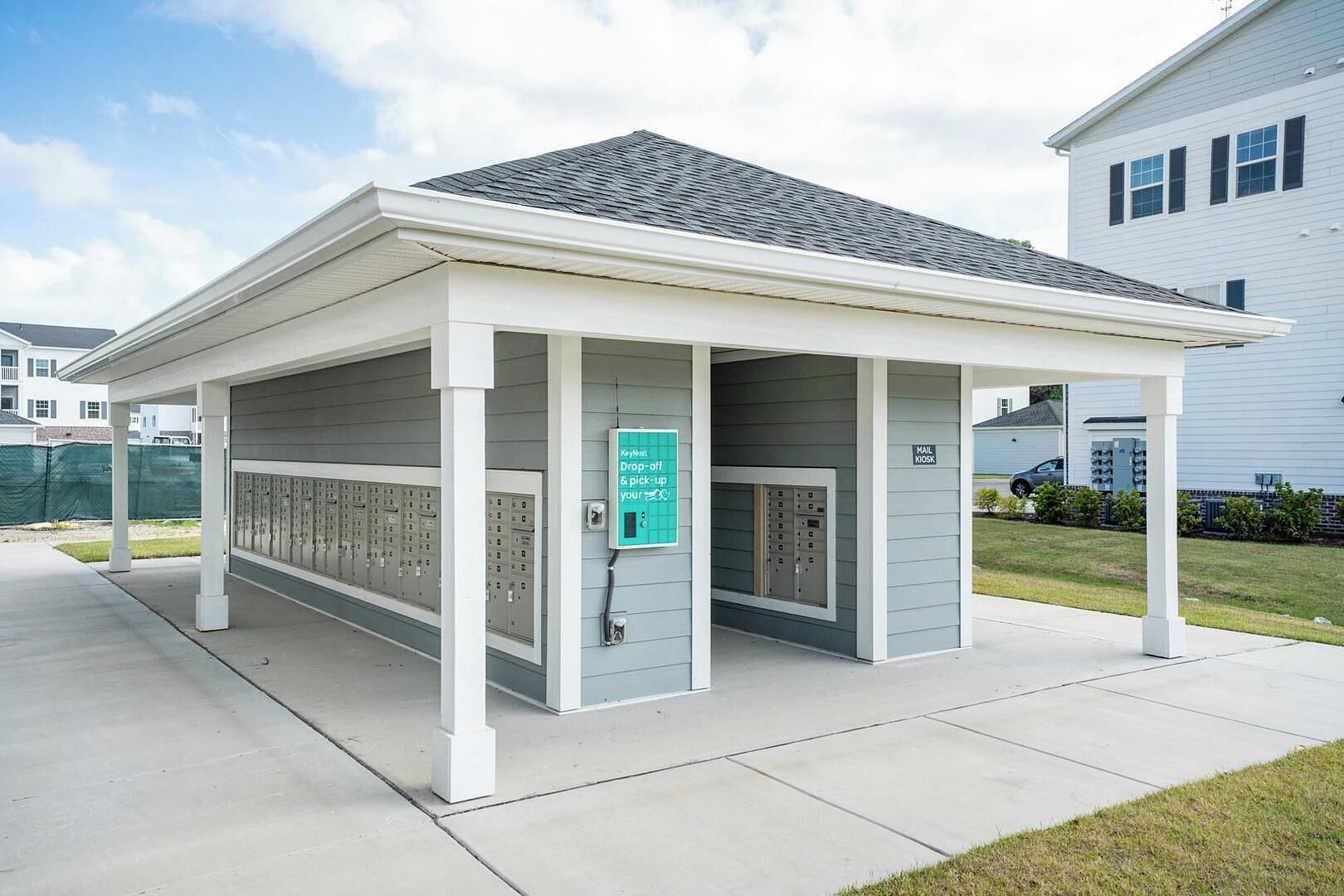 A covered outdoor area with mail and drop-off kiosks, a row of lockers, and a clear sky.
