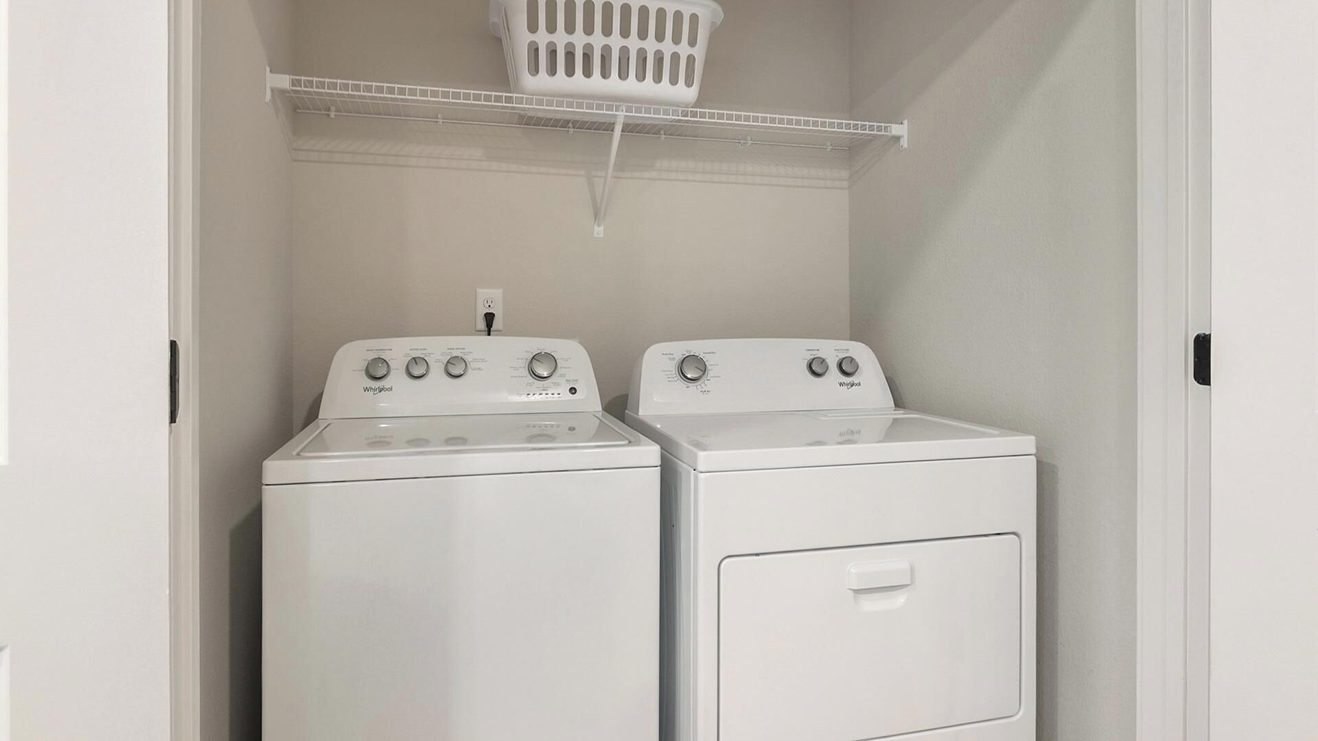 Ein Waschraum mit zwei weißen Whirlpool-Waschmaschinen und einem weißen Wäschekorb auf einem Regal.