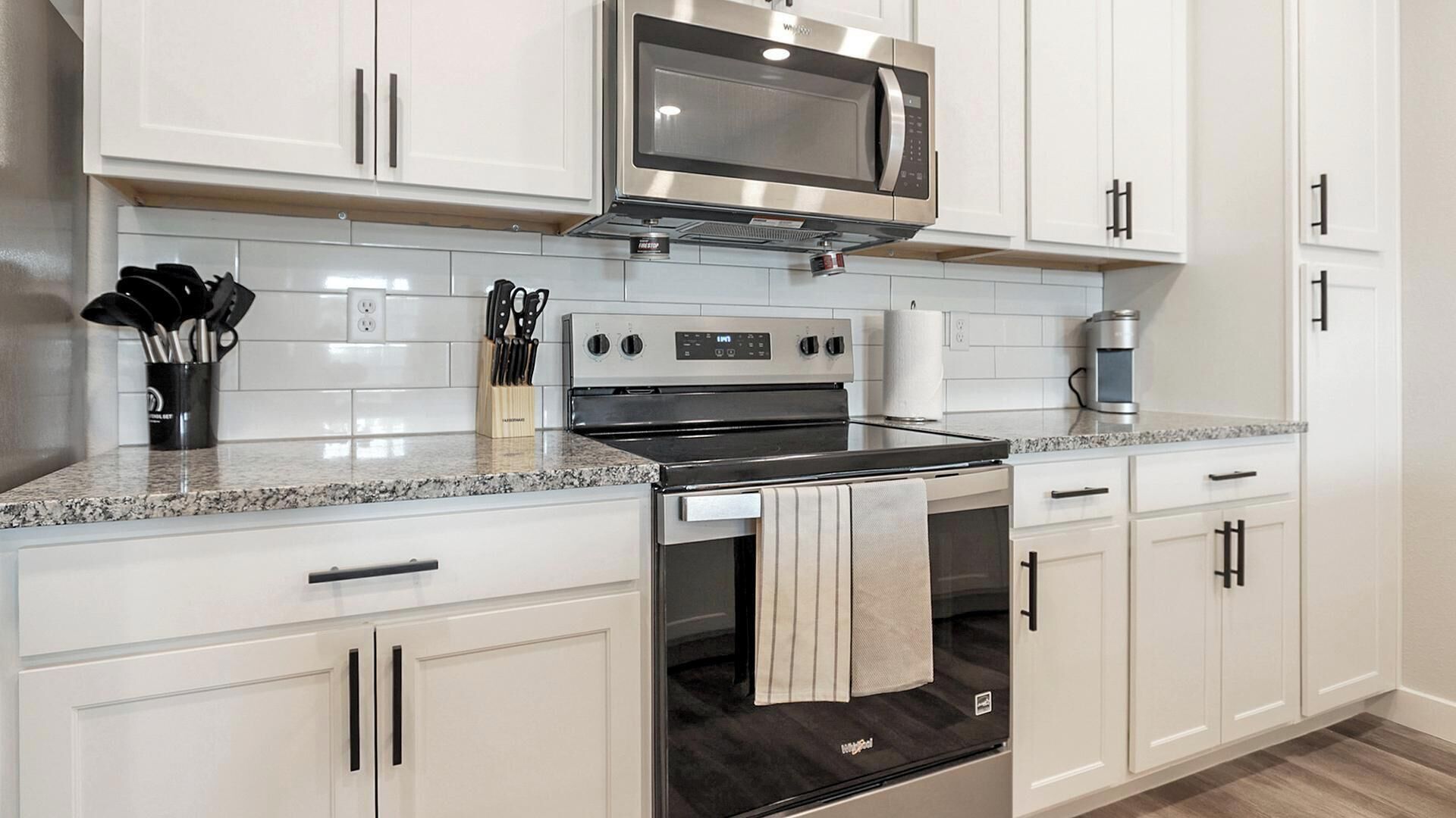 A kitchen with white cabinets, a stainless steel microwave, an oven, and a granite countertop.