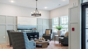Ein Wohnzimmer mit einem großen Gemälde, einer Chandelüster und Blick ins Freie durch die Fenster.