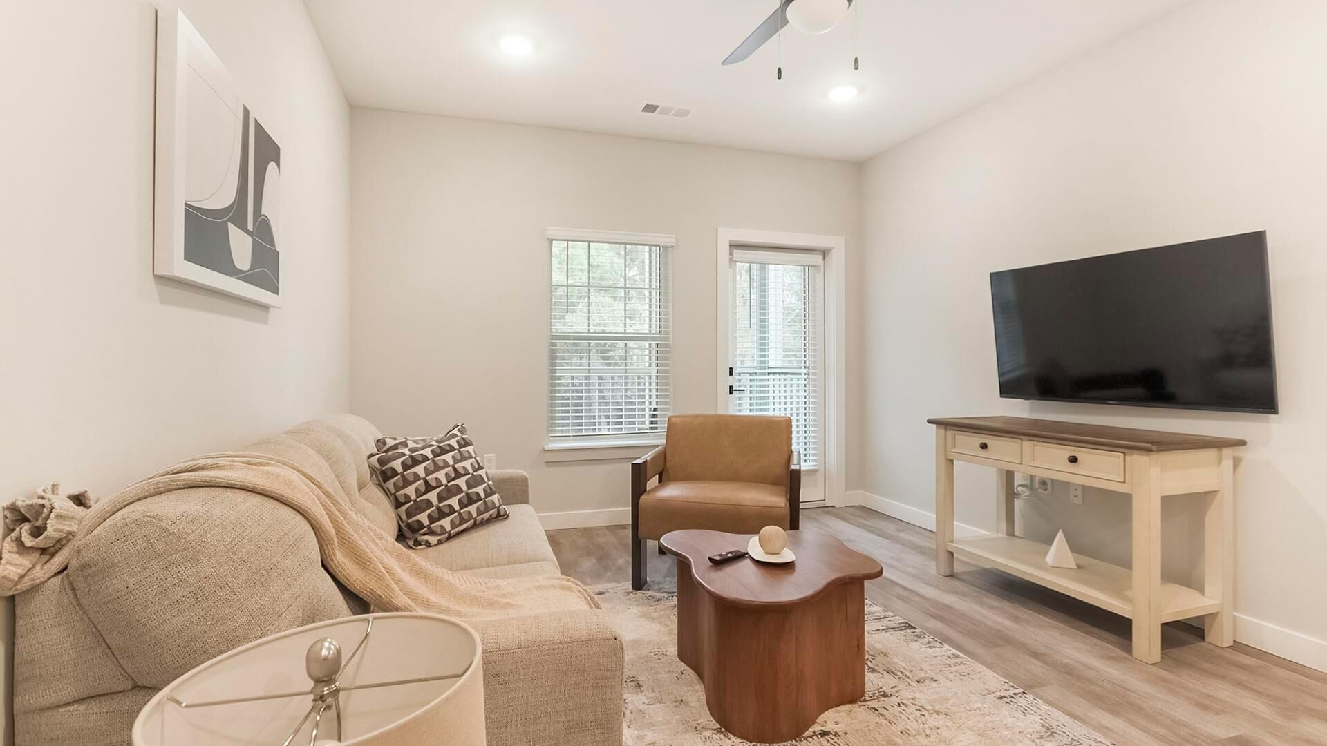 A living room with a sofa, armchair, coffee table, TV, and windows.