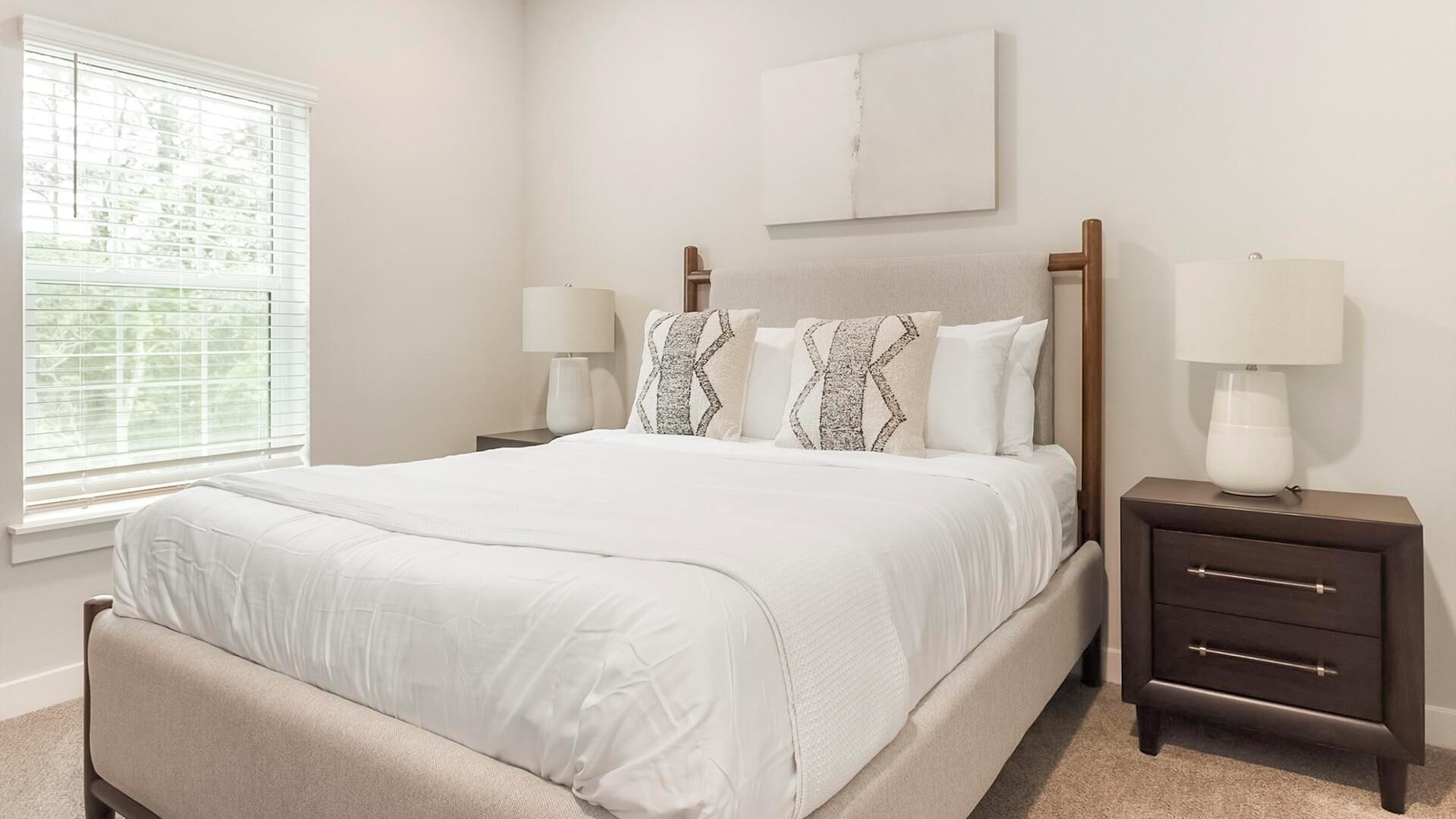 A bedroom with a bed, bedside tables, a window, and a painting on the wall.