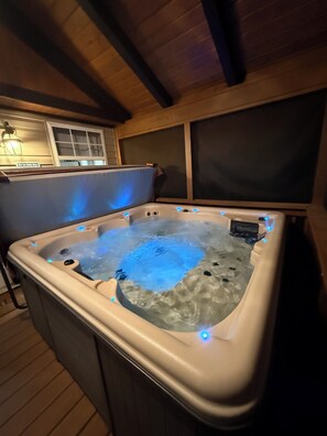 A hot tub with blue LED lights, a wooden ceiling, and a window with blinds.