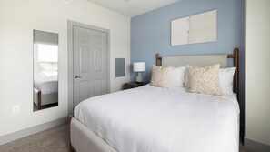 A bedroom with a bed, a nightstand, a lamp, a mirror, and a door. - Landing Amazing 1BD in Grand Prairie (Grand Prairie)