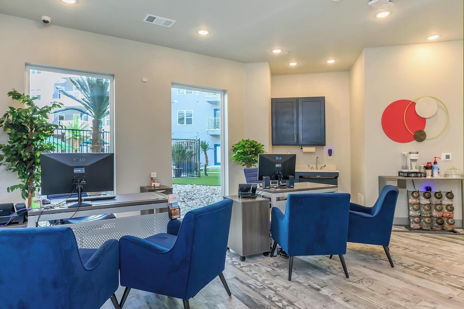 A modern office space with two LG monitors, blue chairs, a reception desk, a plant, and a view of the outside.