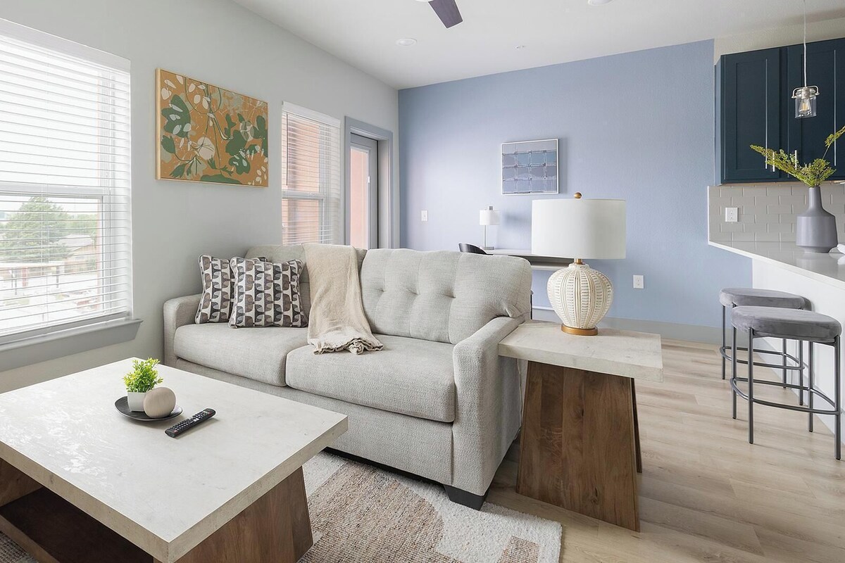 A modern living room with a sofa, a coffee table, and a kitchen area with bar stools.