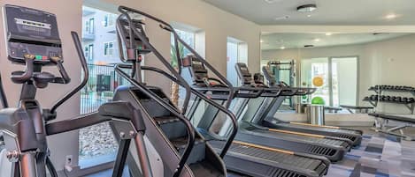 Uma academia com esteiras, bicicleta ergométrica e máquina de remo.
