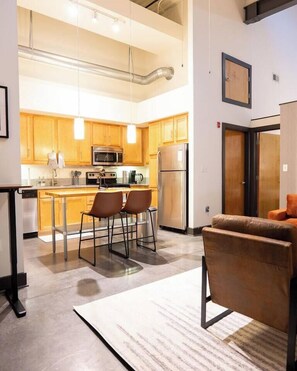 A modern kitchen with stainless steel appliances, wooden cabinets, and a bar area with stools. - Chic Living with Gym, Washer/Dryer, and Work Area (Richmond)