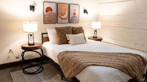 A hotel room with a bed, two bedside lamps, a rug, and artwork on the wall. - Chic Living with Gym, Washer/Dryer, and Work Area (Richmond)