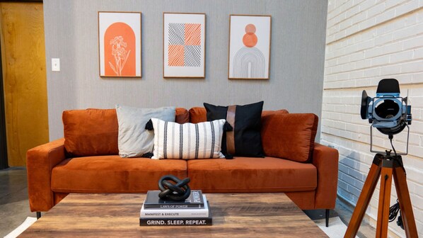 Una sala moderna con sofá, almohadas, una mesita de centro con libros y una cámara sobre un trípode.