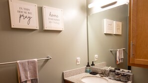 Un baño con toallero, lavamanos, espejo y dos frases inspiradoras enmarcadas en la pared.