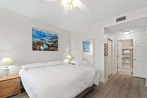 A bedroom with a bed, bedside lamps, a painting, a mirror, and a walk-in closet. - Seaside At Anastrasia A102 Go Coastal (St. Augustine)