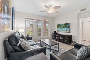 A living room with a sofa set, a coffee table, a TV, and a ceiling fan. - Seaside At Anastrasia A102 Go Coastal (St. Augustine)