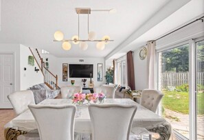 Zona de menjador amb una taula preparada per a sis persones, envoltada de cadires, un penjallum i un televisor al fons.