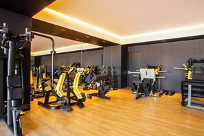 A gym with various exercise equipment, including weight machines and free weights, arranged in a spacious room with wooden flooring and a modern design. - Largest Pool in Zona Romantica at SOHO PV (Puerto Vallarta)