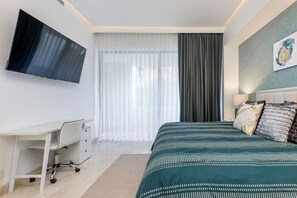 Een slaapkamer met een bed, bureau, stoel, televisie en een raam met gordijnen.