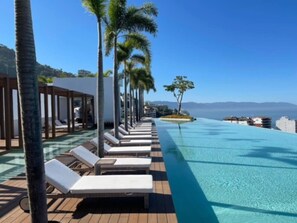 A poolside area with lounge chairs and palm trees, overlooking a clear blue pool. - Largest Pool in Zona Romantica at SOHO PV (Puerto Vallarta)