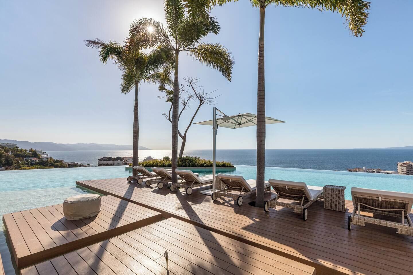 A wooden deck with lounge chairs and a pool overlooking the sea.