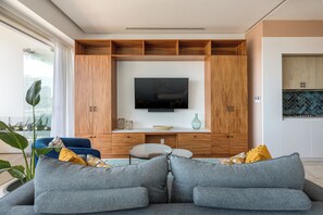 Een moderne woonkamer met een flatscreen televisie, houten kasten, een bank en een eettafel.