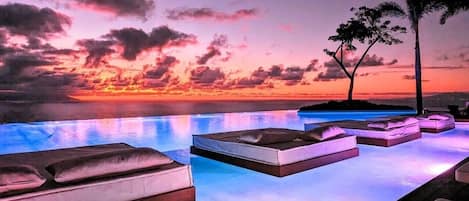 An infinity pool with lounge chairs and a sunset view.