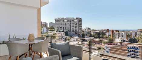 A balcony with wicker furniture, a table, and a view of the cityscape.
