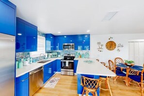 Eine moderne Küche mit blauen Schränken, Edelstahlgeräten und einem Essbereich mit Korbstühlen und einem weißen Tisch.