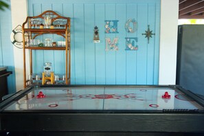 A room with a blue wall, a welcome sign, a life preserver, a wooden shelf with glassware, and a table with a logo. - Gulf-to-Atlantic Waterfront Escape — Pool, Tiki Bar & Endless Fun (Marathon)