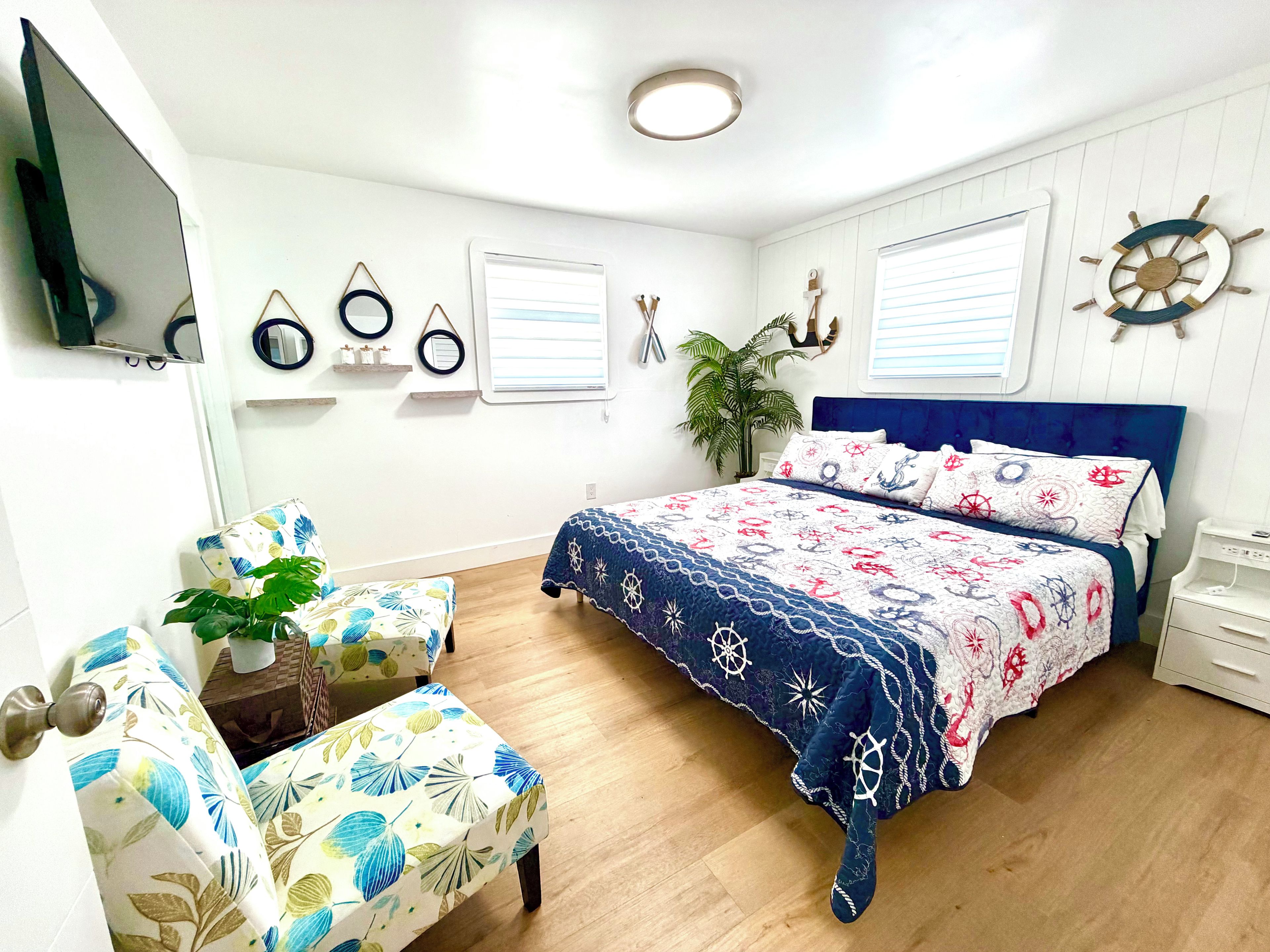 Une chambre à coucher avec un lit, une chaise, un bureau, une plante et un téléviseur fixé au mur.