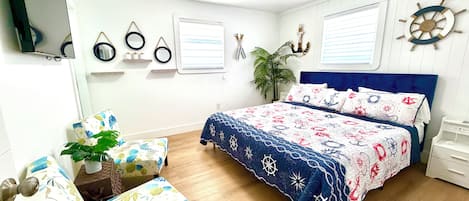 Une chambre à coucher avec un lit, une chaise, un bureau, une plante et un téléviseur fixé au mur.