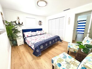 A bedroom with a bed, a nightstand, a potted plant, a wardrobe, and a door leading to another room. - Gulf-to-Atlantic Waterfront Escape — Pool, Tiki Bar & Endless Fun (Marathon)
