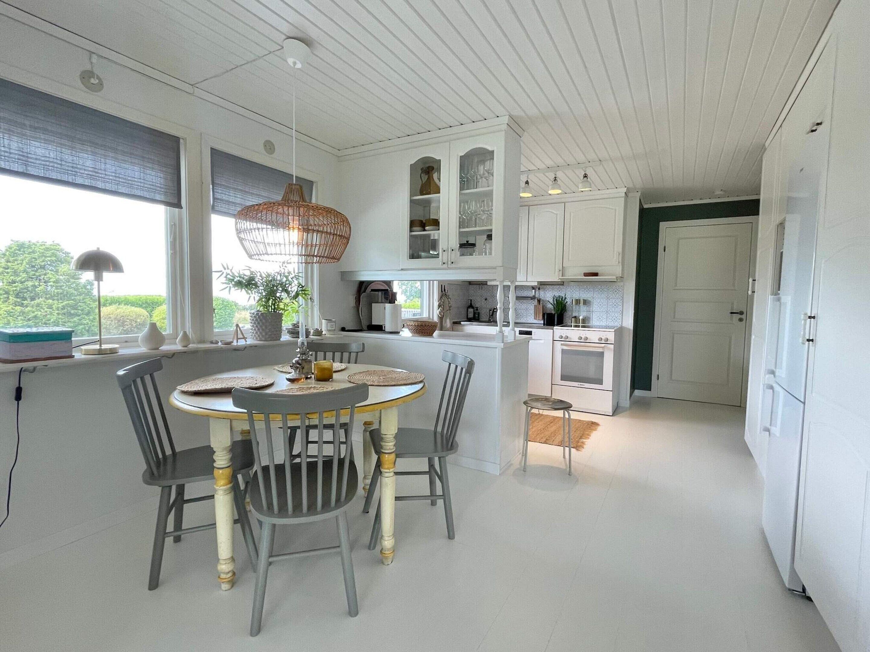 A kitchen with white cabinetry, a dining table with chairs, and a hanging light fixture.