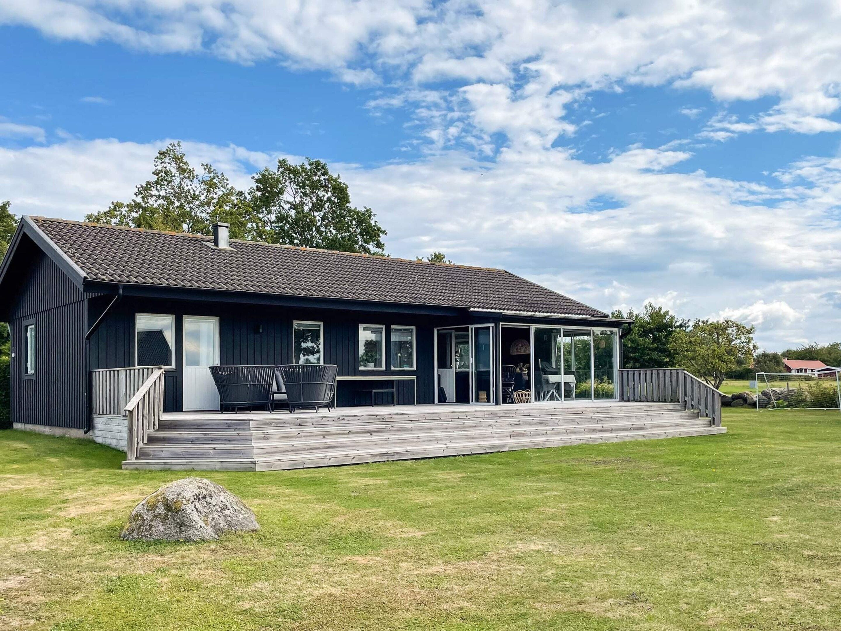 A modern house with a covered porch, a lawn, and a large rock in the foreground.