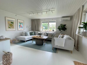 A modern living room with a sofa, armchairs, a coffee table, and a dining table. There are framed pictures on the wall, a plant, and a window with curtains. - 8 Person Holiday Home in Kopingsvik (Kopingsvik)