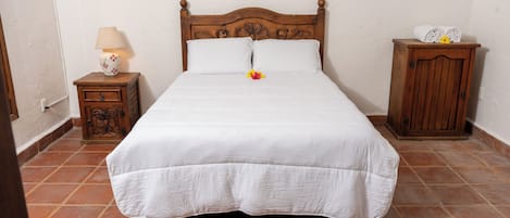 Una cama bien hecha con cabecera de madera, una mesita de noche con lámpara y un pequeño armario.