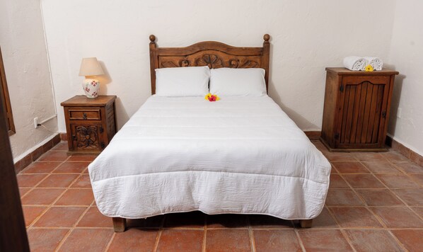 A neatly made bed with a wooden headboard, a bedside table with a lamp, and a small cabinet.