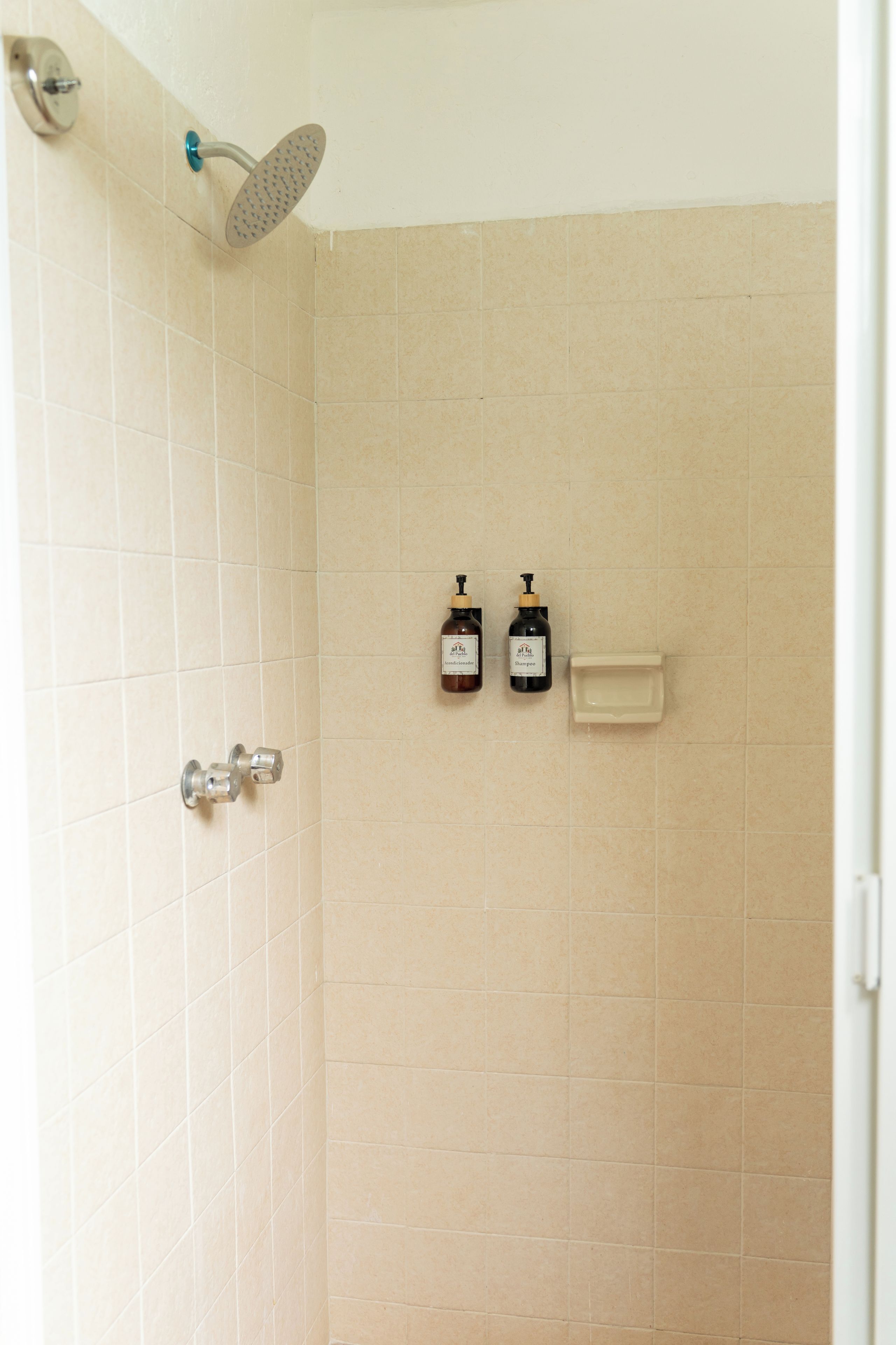 Ducha con cabezal de ducha de mano, grifo empotrado en la pared y dos botellas de champú y acondicionador.