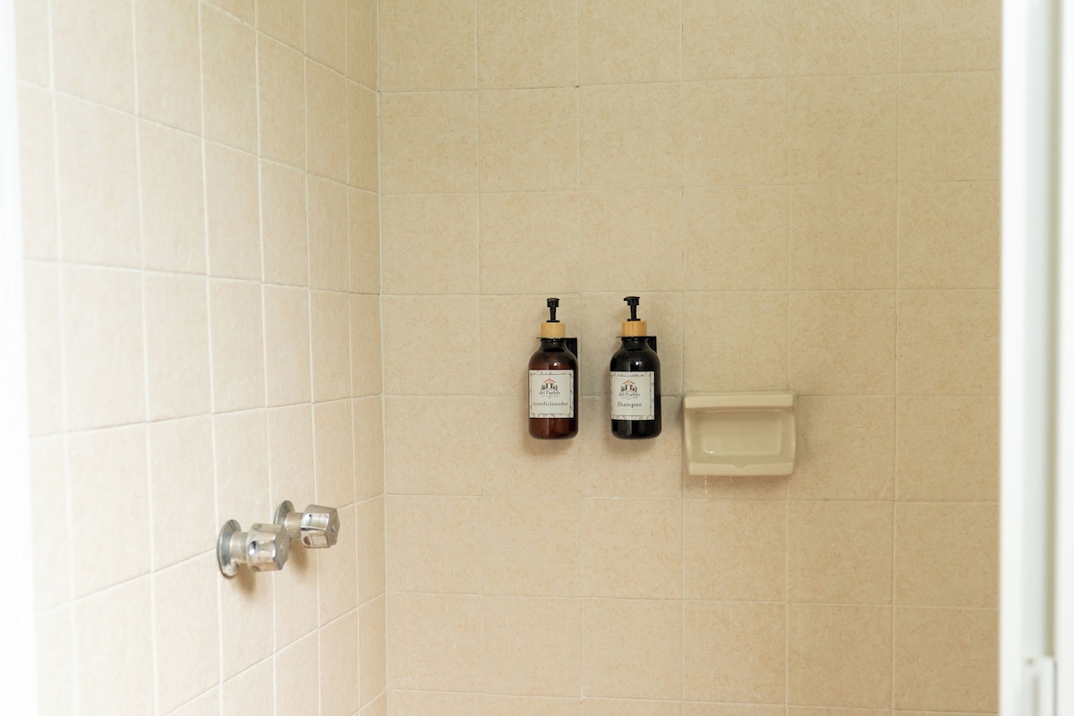 A shower with a handheld showerhead, a wall-mounted faucet, and two bottles of shampoo and conditioner.