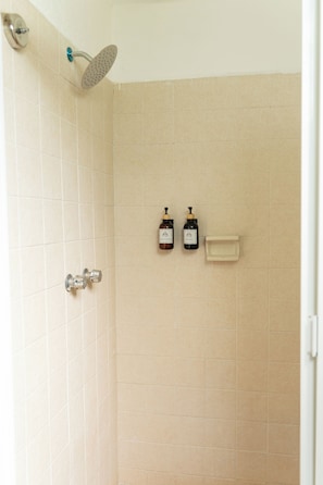 Ducha con cabezal de ducha de mano, grifo empotrado en la pared y dos botellas de champú y acondicionador.