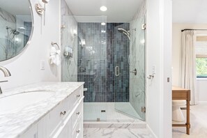 Un baño moderno con ducha de vidrio, encimeras de mármol y un espejo grande.
