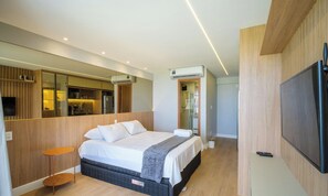 A modern hotel room with a bed, a TV, a mirror, and a kitchenette. - Studio With Balcony and sea View - Rgf1201 (Salvador)