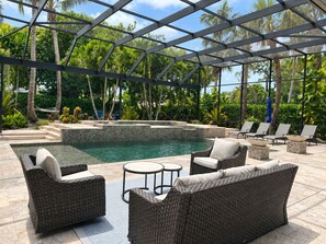 An outdoor pool area with wicker furniture, a hot tub, and a covered seating area.