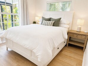 A bedroom with a large bed, a nightstand with a lamp, and a window with blinds.