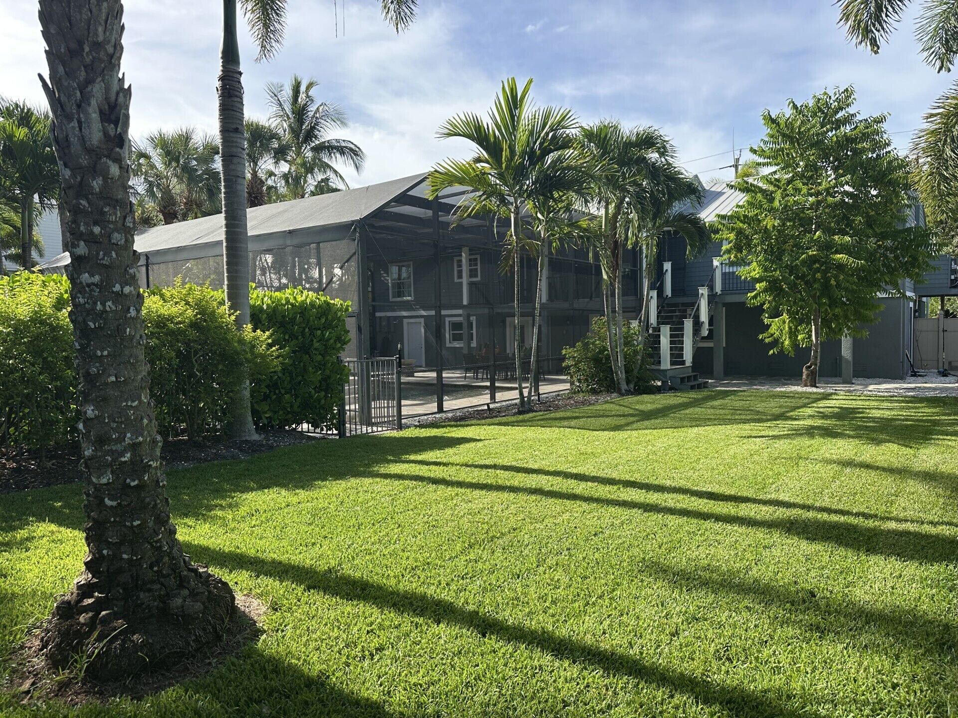 A residential area with a well-maintained lawn, a house with a large balcony, and a clear sky.